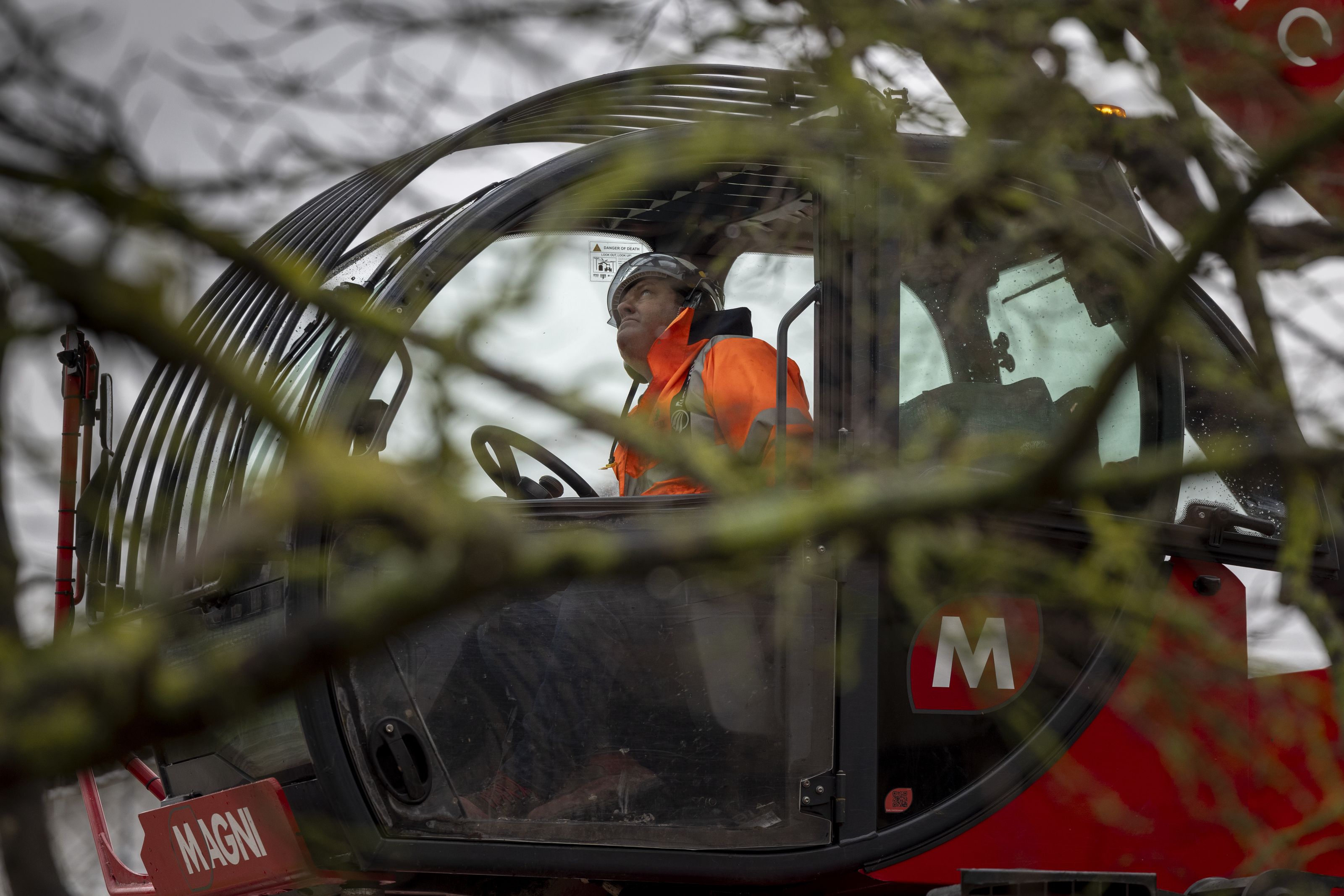 A man behind the wheel of a telehandler wearing an orange jacket looks up