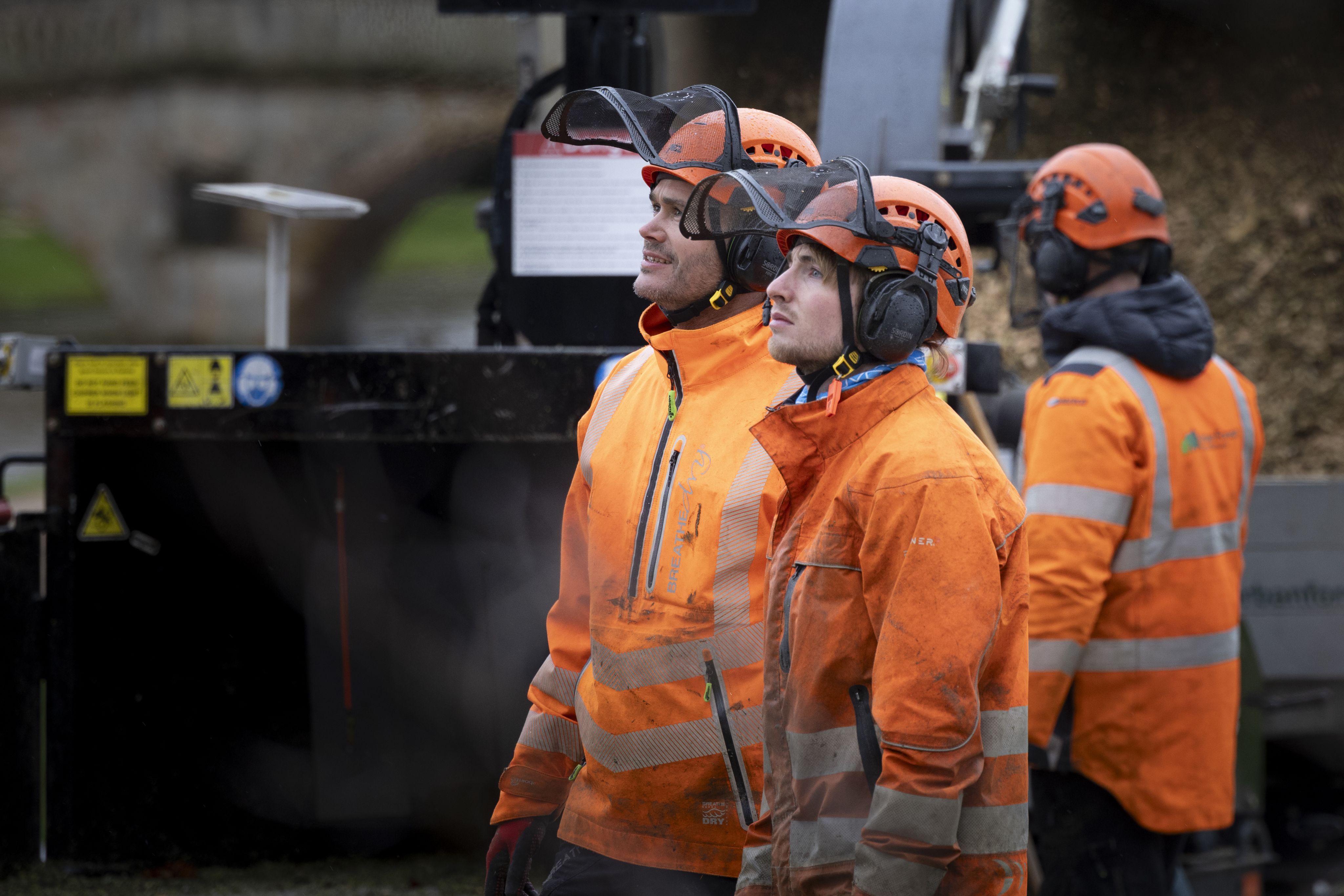Several workers in orange hats and jackts stand in front of machinery
