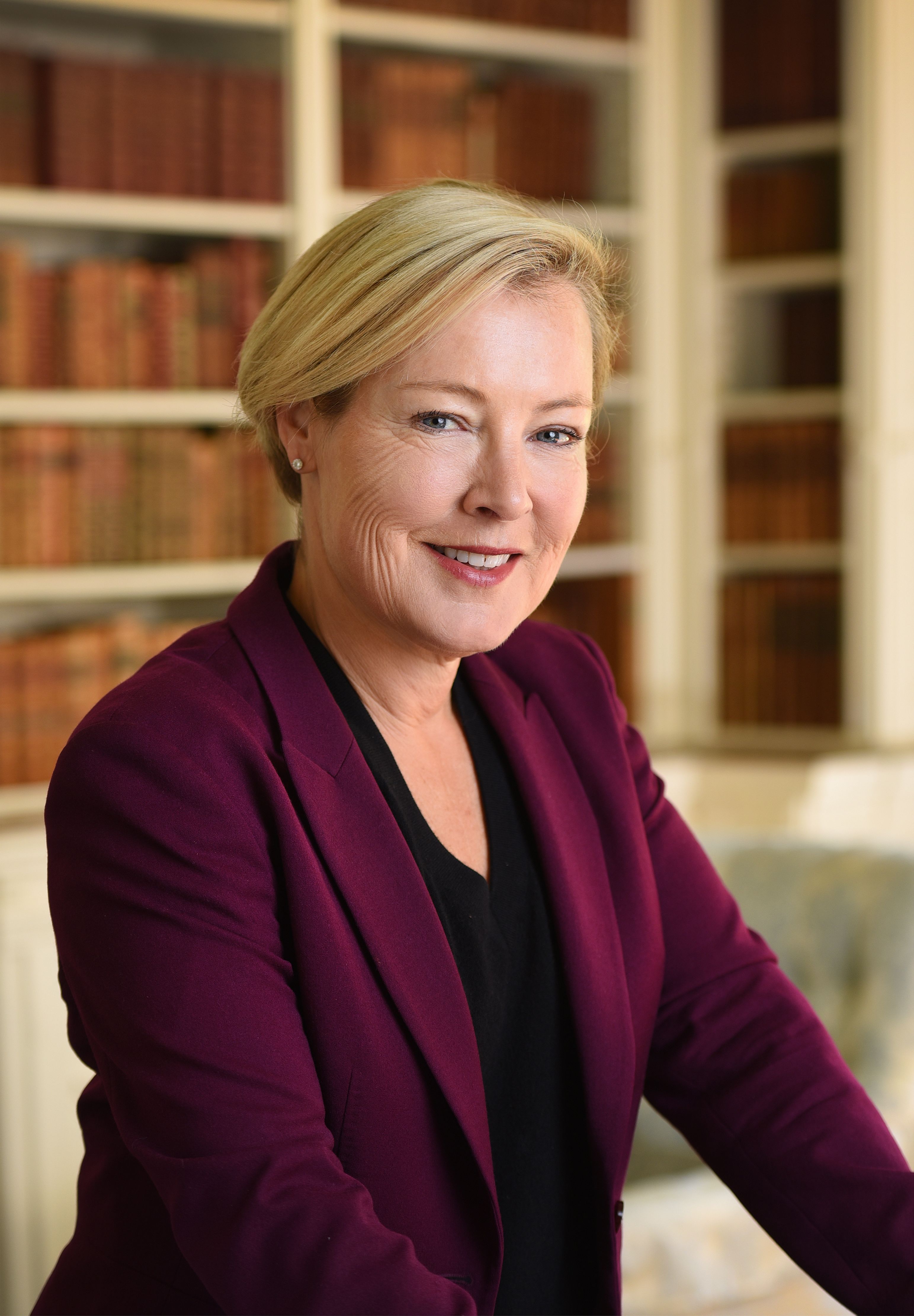 A woman in a plum jacket in front of a book case