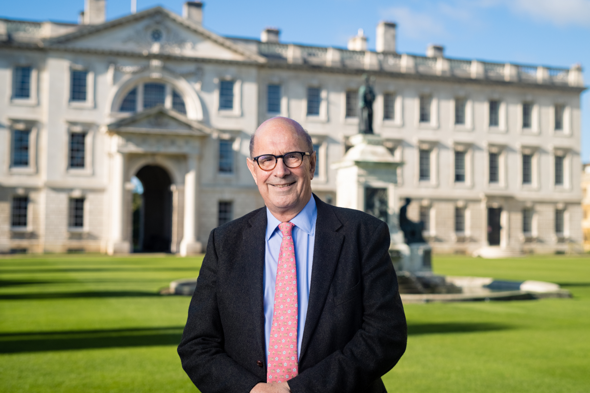A white man with glasses in front of a lawn and historic building